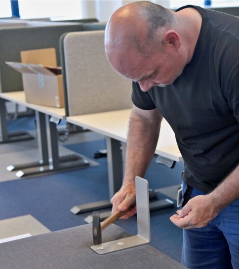 Muž zatlouká kladivem šrouby k polohovatelnému stolu